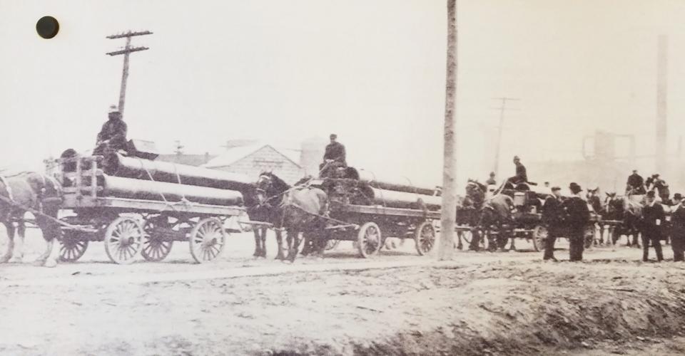 Cast Iron Pipe being delivered with horse drawn carts.
